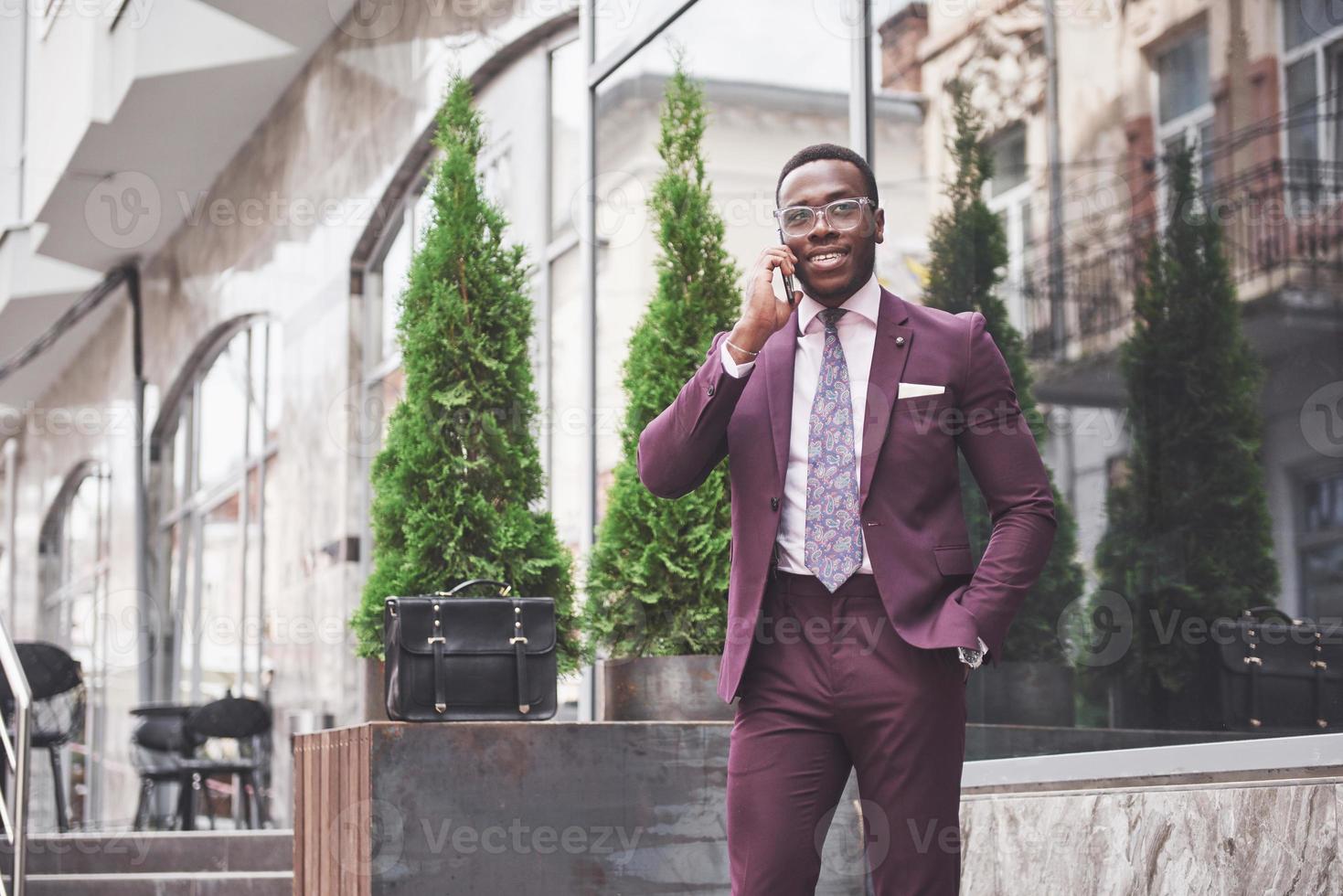 porträtt av en ung och stilig afroamerikansk affärsman som pratar i kostym över telefon. förbereder sig för ett affärsmöte. foto