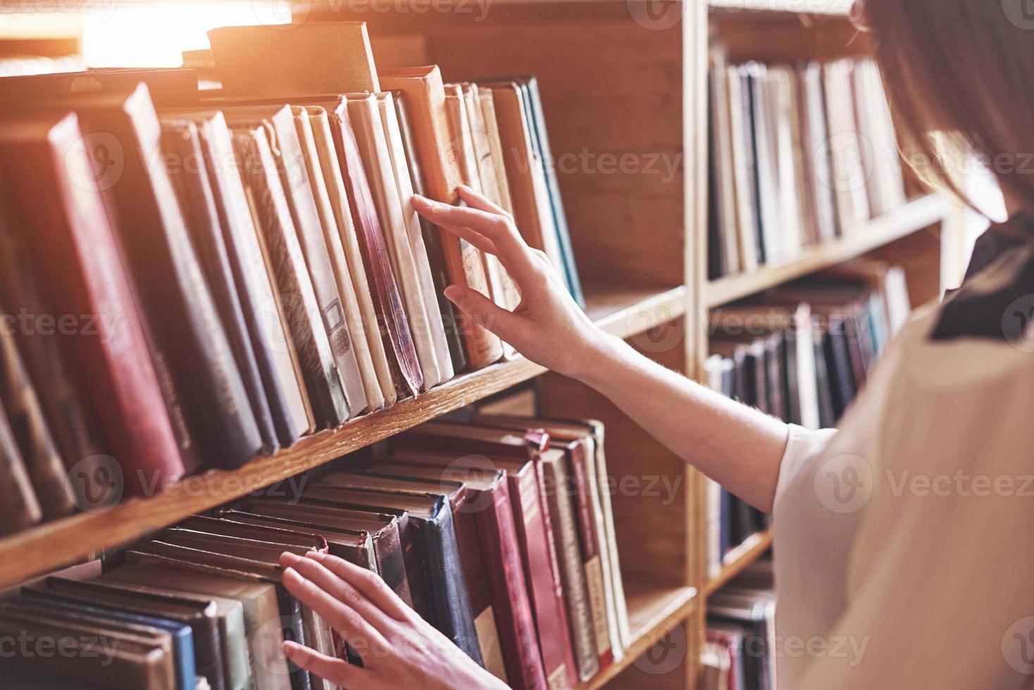 ung attraktiv studentbibliotekarie som läser en bok mellan bibliotekets bokhyllor foto