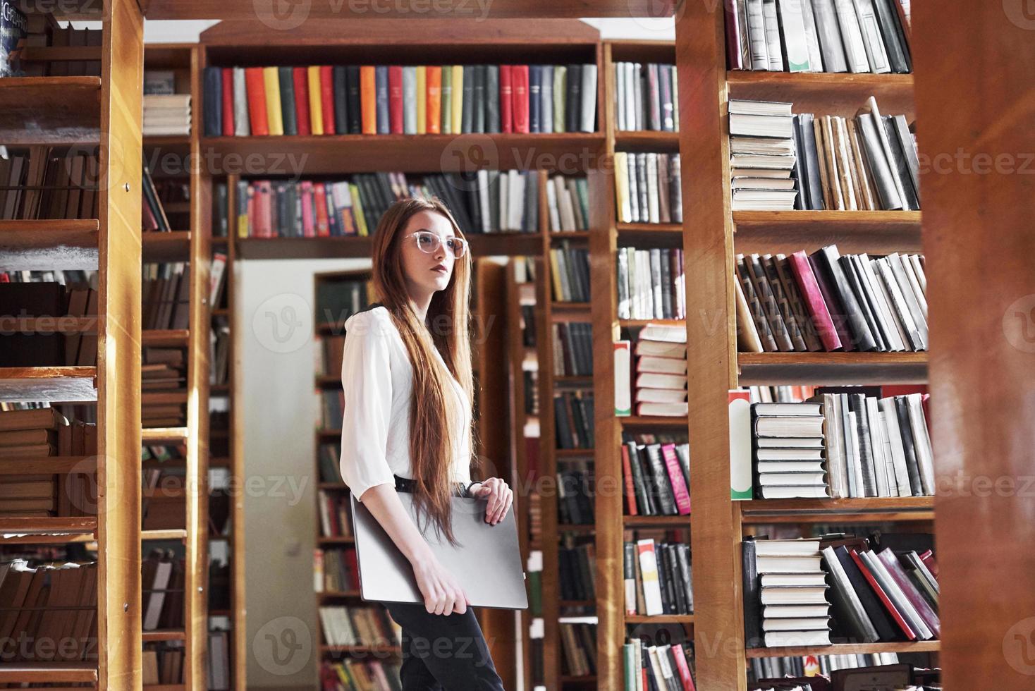 ung vacker kvinna är en student på ett bibliotek med sin bärbara dator foto