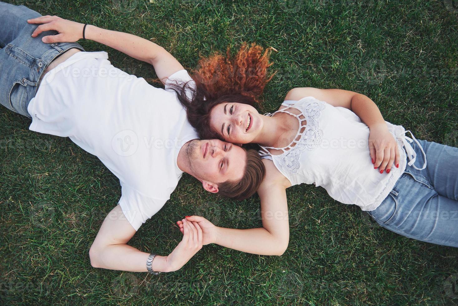 romantiska par unga människor som ligger på gräs i parken. de ser lyckliga ut. vy uppifrån. foto