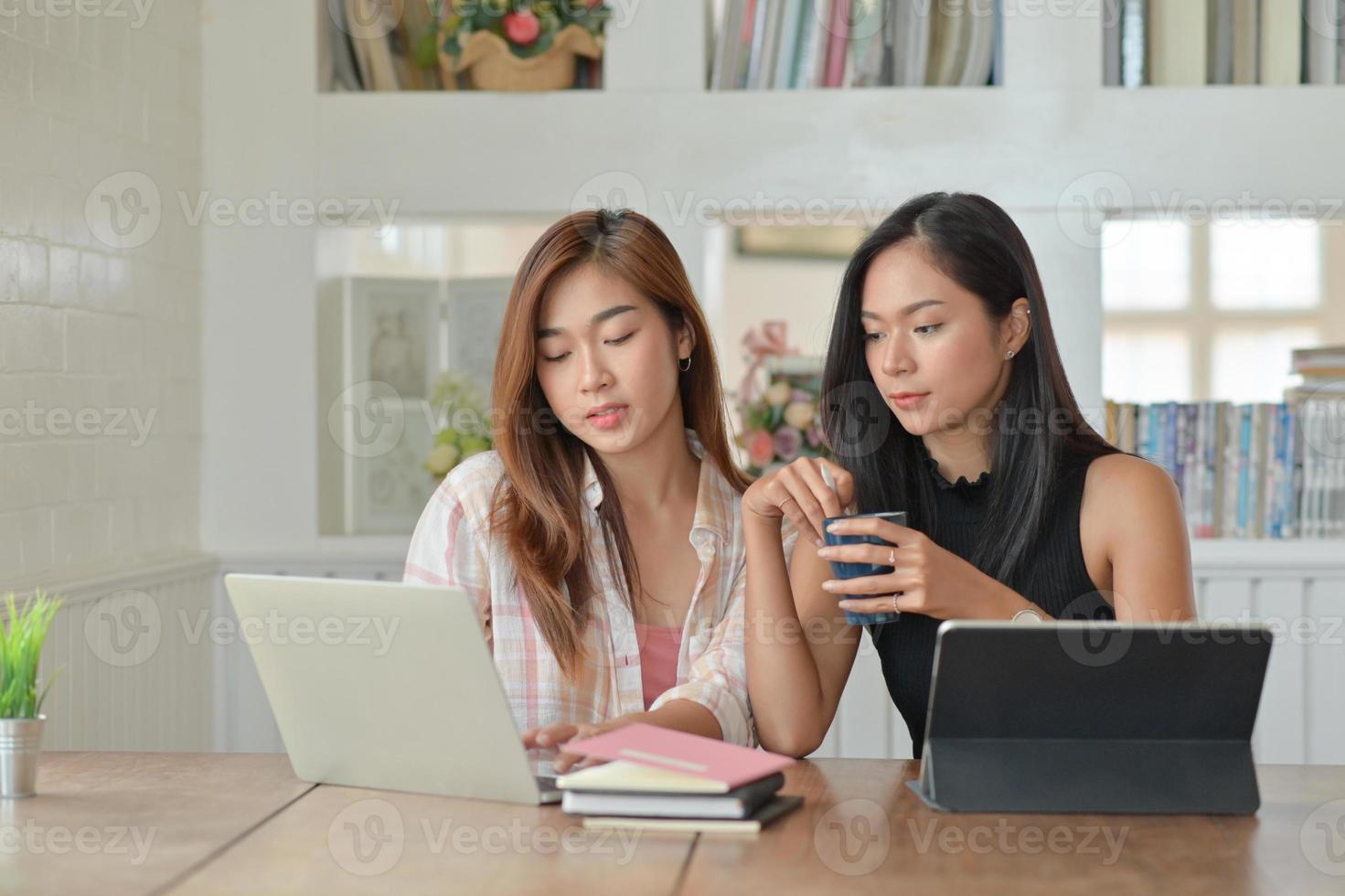 två unga kvinnliga studenter med kaffe använder en bärbar dator för att studera online hemma under sommarsemestern. foto