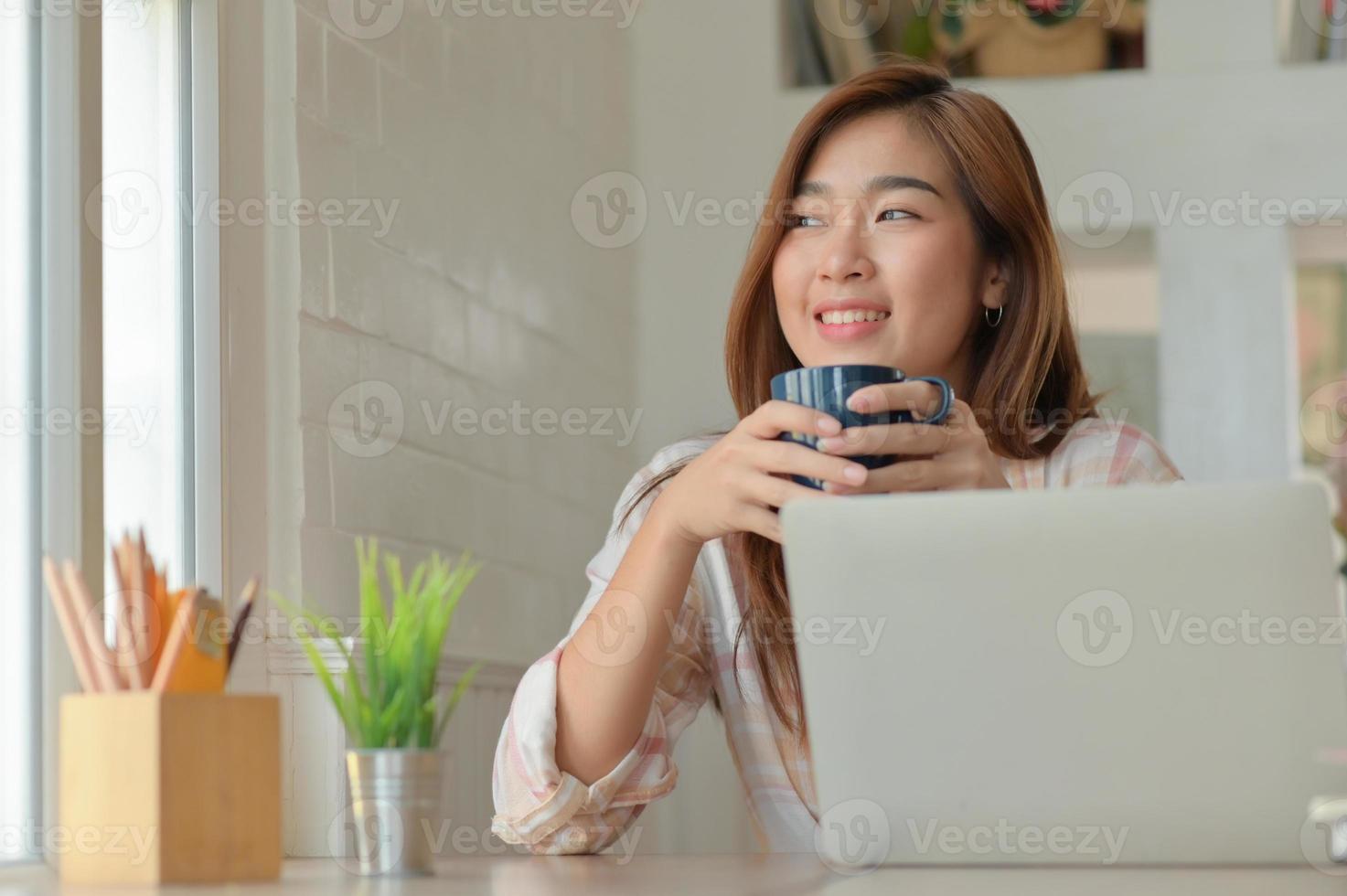 ett porträtt av en asiatisk kvinna ler glatt med en kaffekopp under en paus från arbetet på ett bekvämt kontor. foto