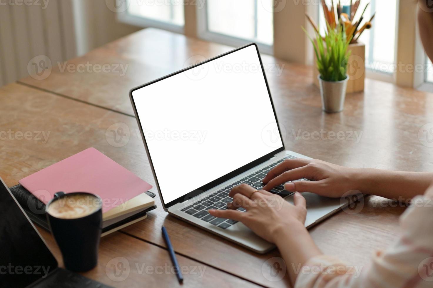 handen av en kvinnlig student som använder ett bärbart tangentbord för att hitta information om att studera med kaffe och böcker på skrivbordet. foto