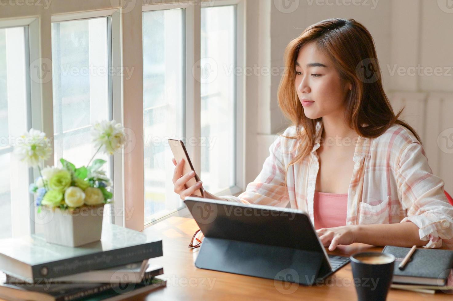 ett porträtt av en asiatisk kvinnlig student använder en smartphone och en bärbar dator för att förbereda högskoleexamen. foto
