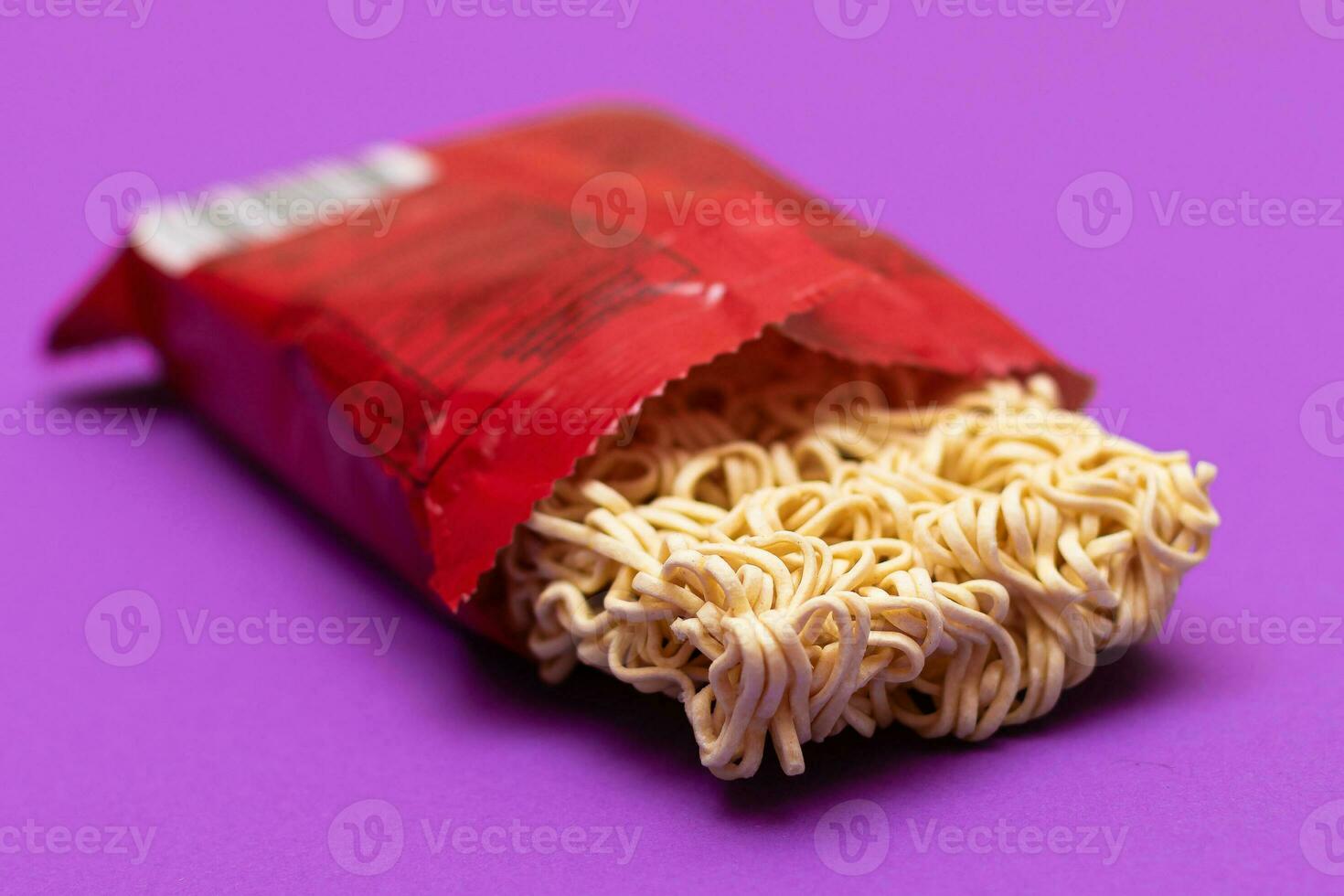 öppnad paket med okokt omedelbar spaghetti på violett bakgrund. rå pasta. torr asiatisk snabb mat. snabbt lunch foto