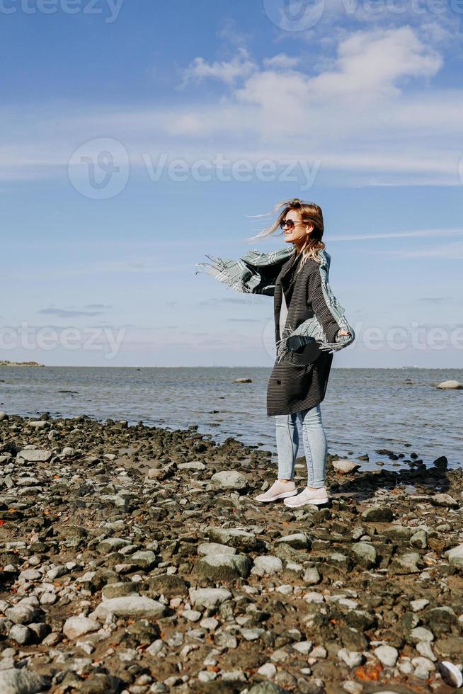 ung kvinna i solglasögon insvept i halsduk, höst vid Finlands viken foto