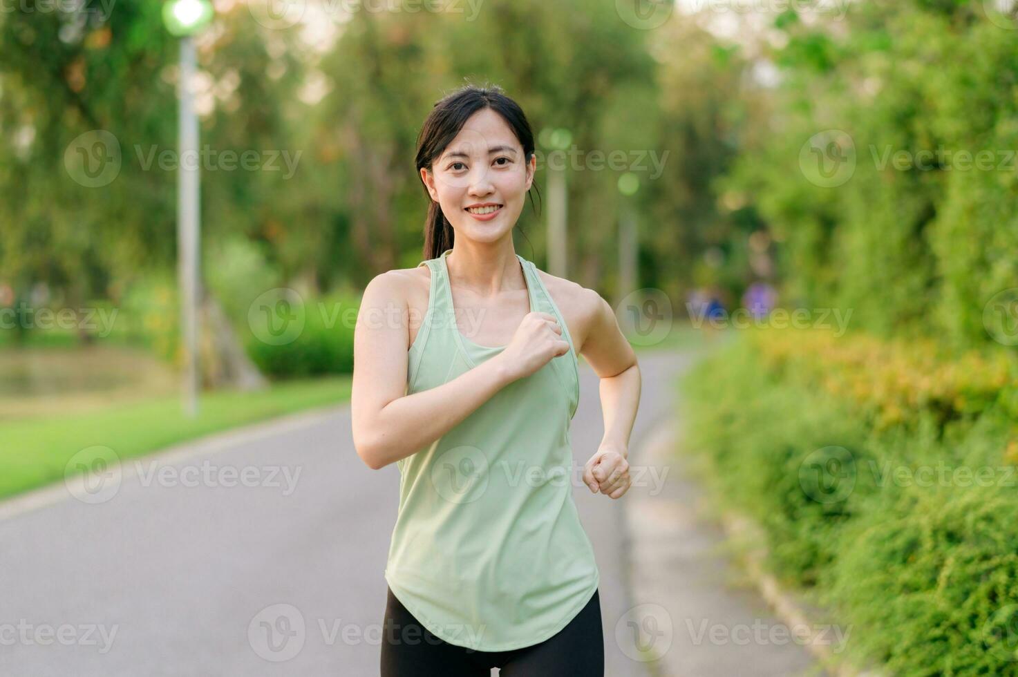 passa asiatisk ung kvinna joggning i parkera leende Lycklig löpning och njuter en friska utomhus- livsstil. kvinna joggare. kondition löpare flicka i offentlig parkera. friska livsstil och wellness varelse begrepp foto