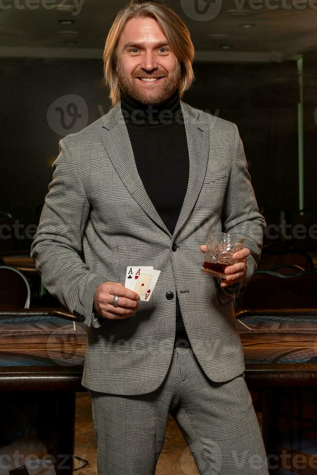 glad man med par av ess och glas av dryck stående nära poker tabell i kasino foto