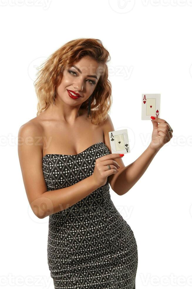 ingefära flicka bär grå klänning är Framställ innehav två spelar kort i henne händer stående isolerat på vit bakgrund. kasino, poker. närbild skott. foto