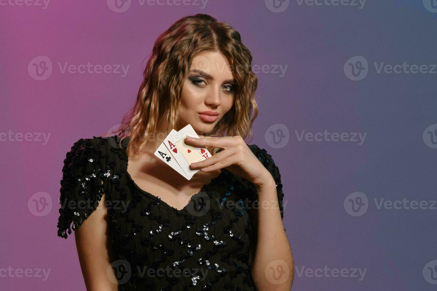 brunhårig jungfru med lockigt hår, i svart klänning som visar två ess, Framställ på färgrik bakgrund. hasardspel underhållning, poker, kasino. närbild. foto
