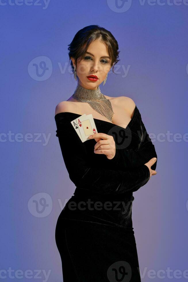 brunett kvinna med bar axlar, i svart klänning och skinande Smycken. som visar två ess, Framställ mot lila bakgrund. poker, kasino. närbild foto