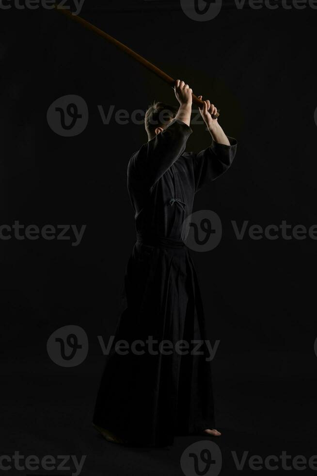 kendo guru bär i en traditionell japansk kimono är praktiserande krigisk konst med de shinai bambu svärd mot en svart studio bakgrund. foto