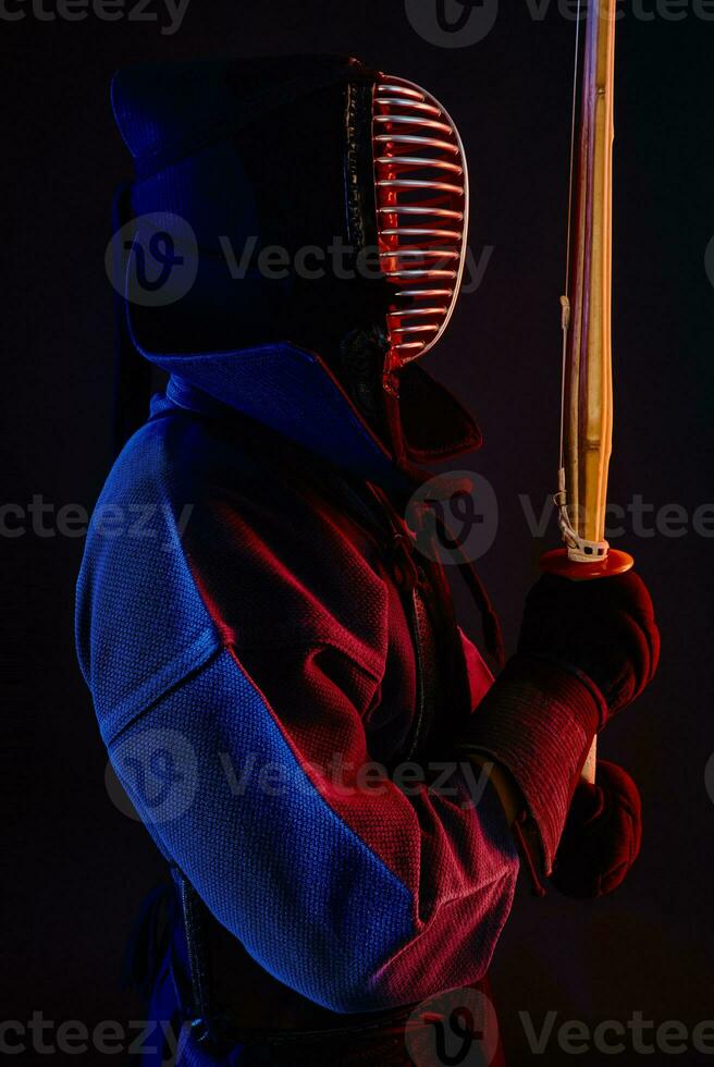 stänga upp skott, kendo kämpe bär i ett rustning, traditionell kimono, hjälm praktiserande krigisk konst med shinai bambu svärd, svart bakgrund. foto