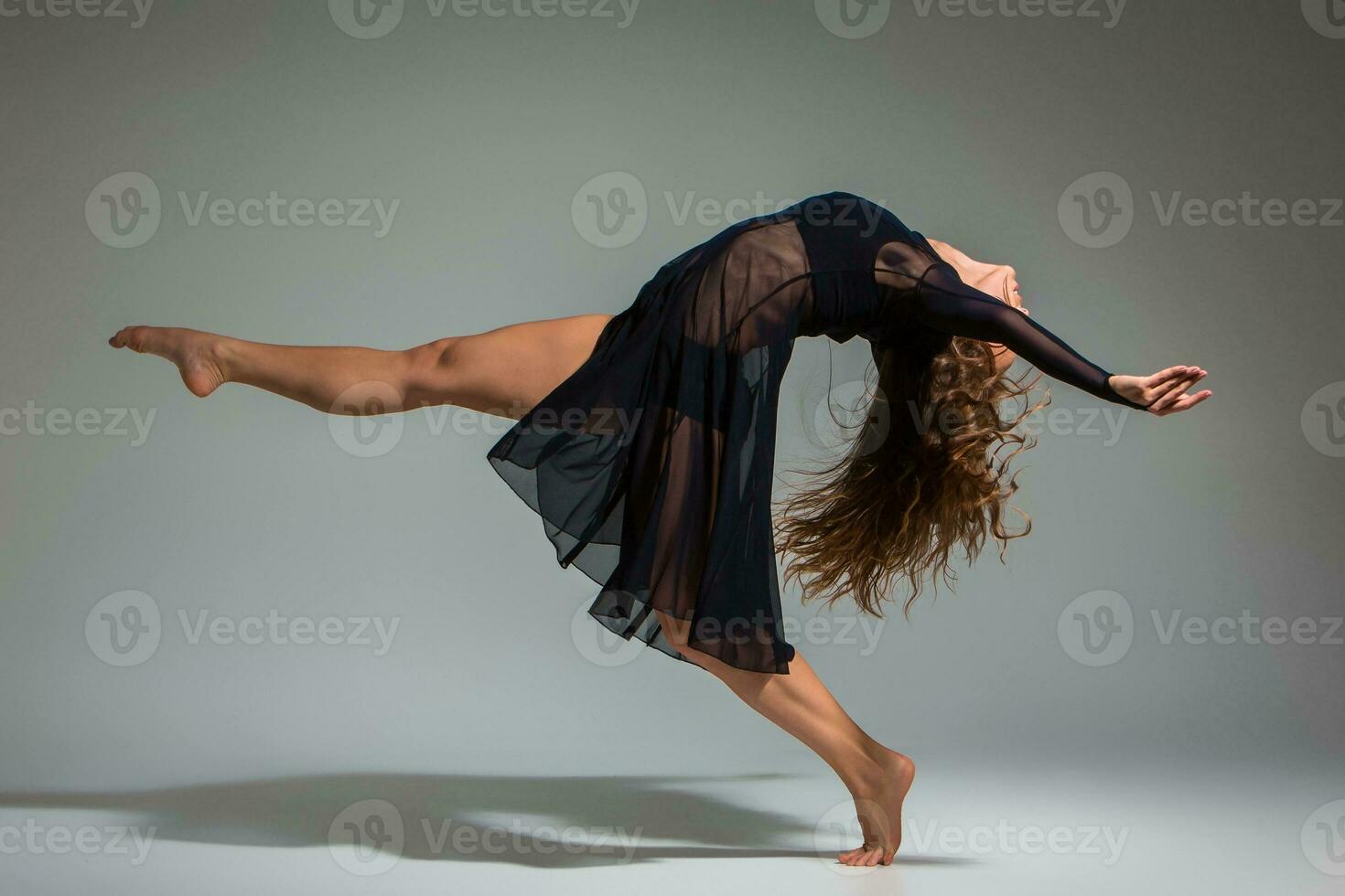 ung skön dansare i svart klänning Framställ på en mörk grå studio bakgrund foto