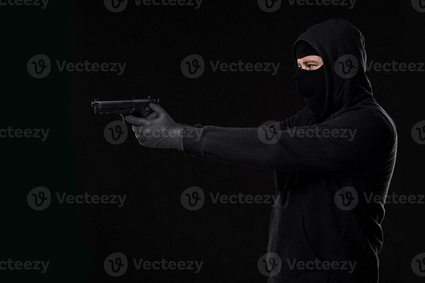 de rånare i en mask med en pistol spetsig till de sida på en svart bakgrund foto