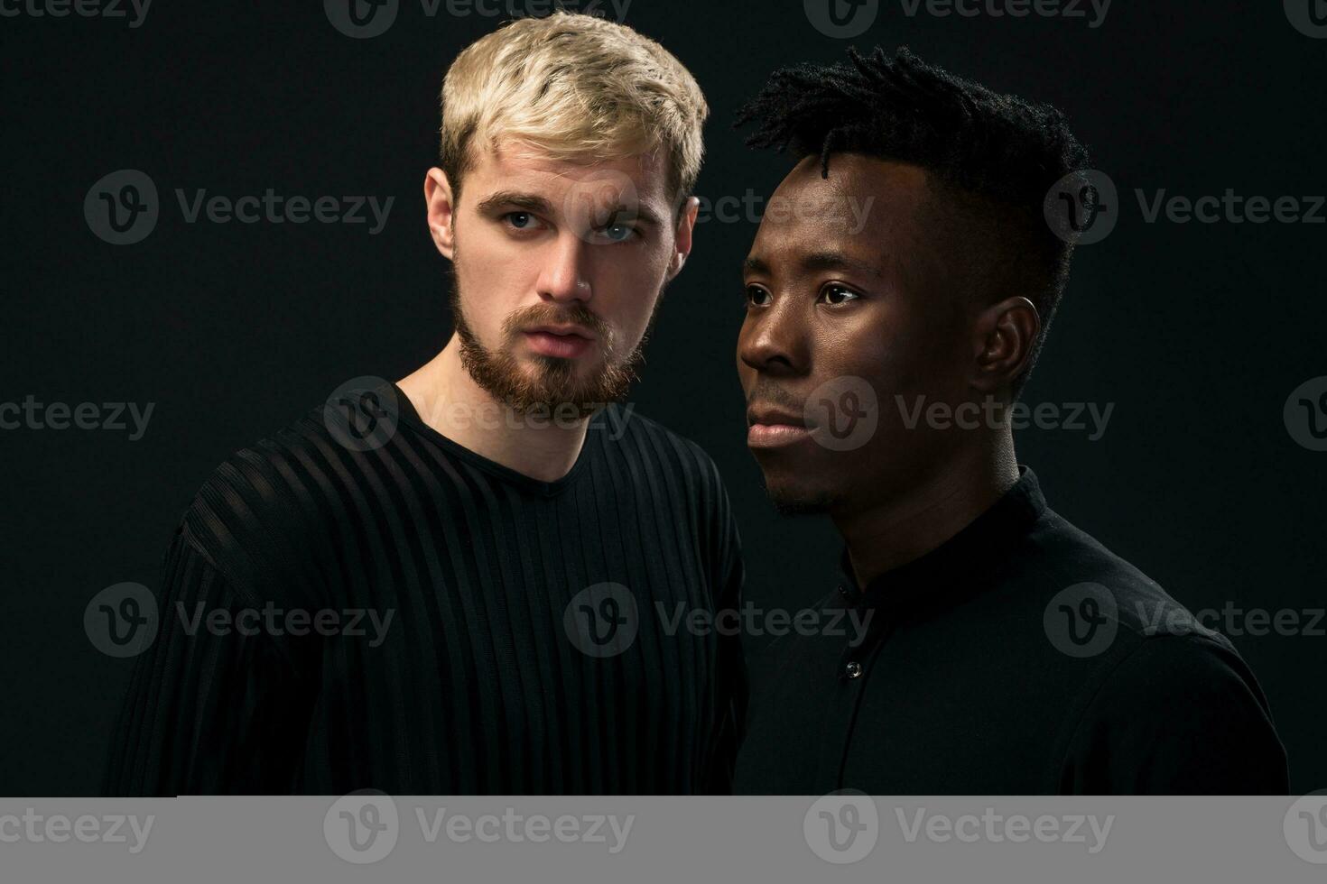 porträtt av två ung afrikansk amerikan och caucasian män stående över svart bakgrund. studio skott foto