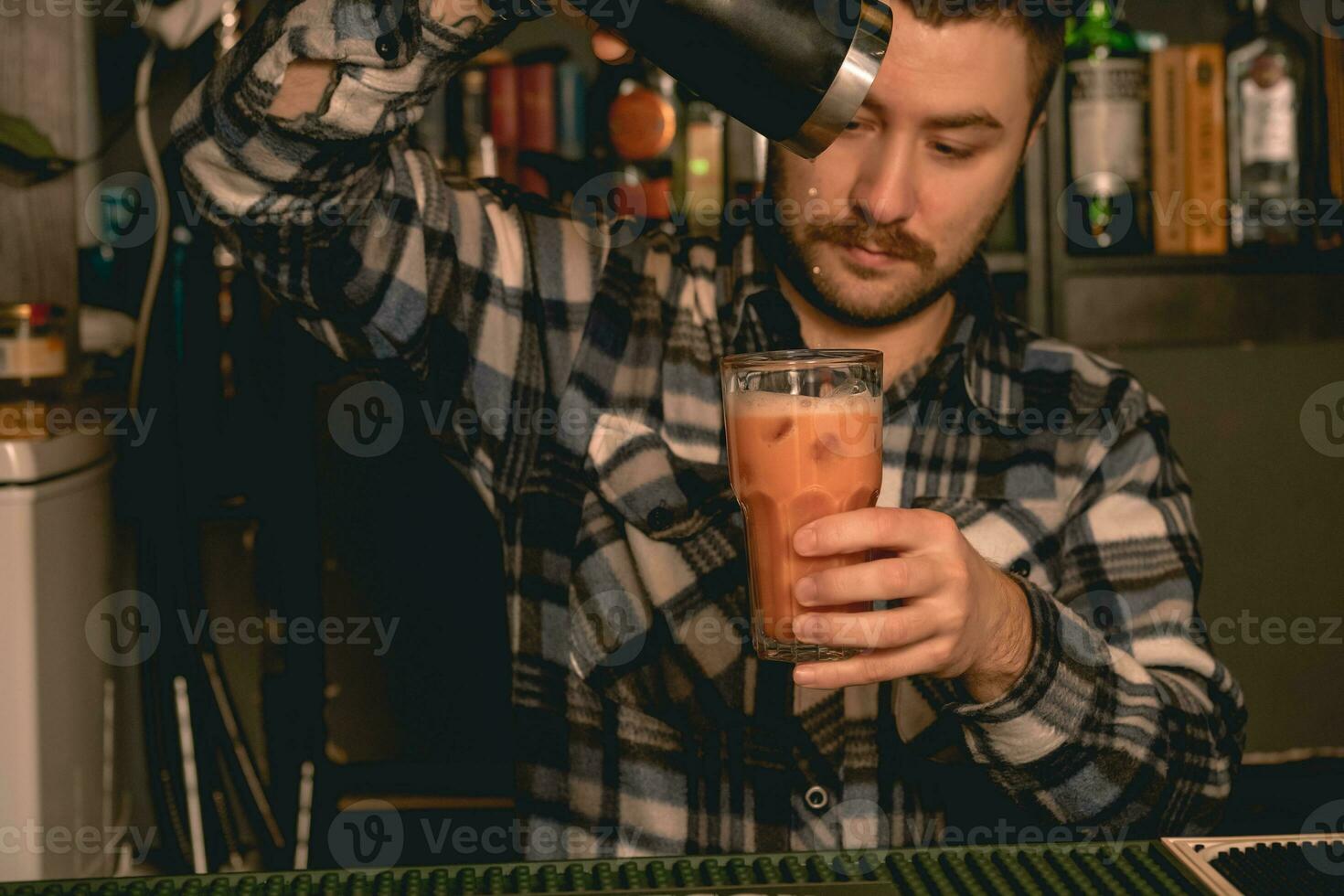 skäggig bartender häller cocktail från shaker in i grogg glas foto