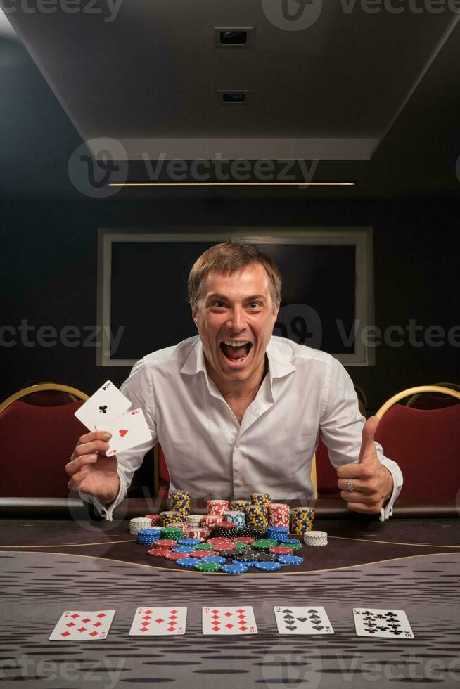 stilig emotionell man är spelar poker Sammanträde på de tabell i kasino. foto