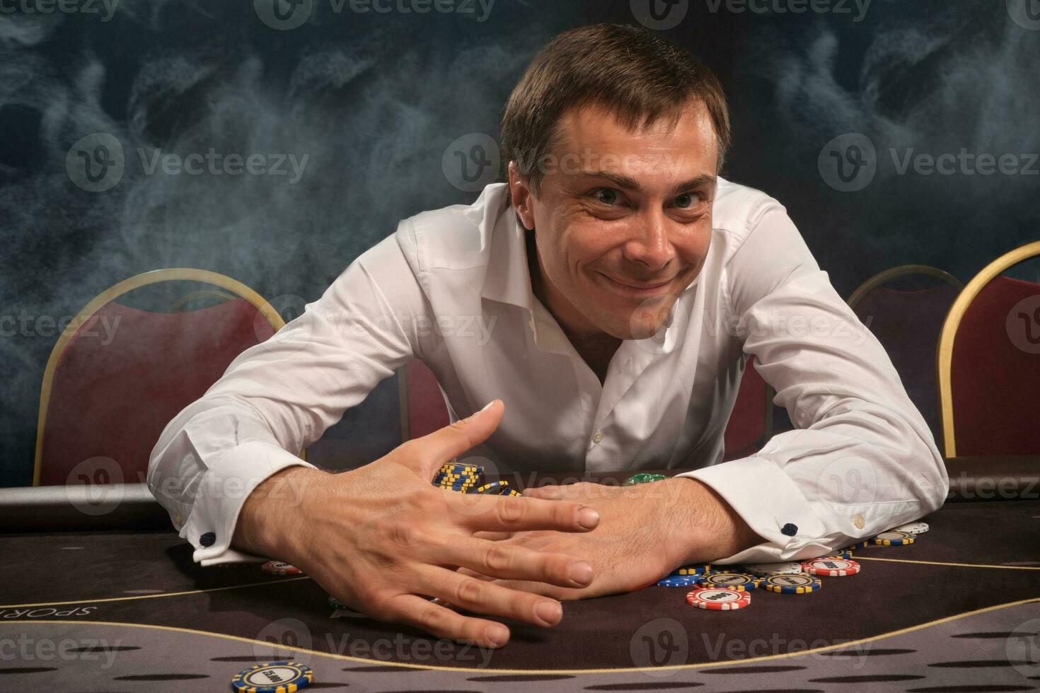 stilig emotionell man är spelar poker Sammanträde på de tabell i kasino. foto