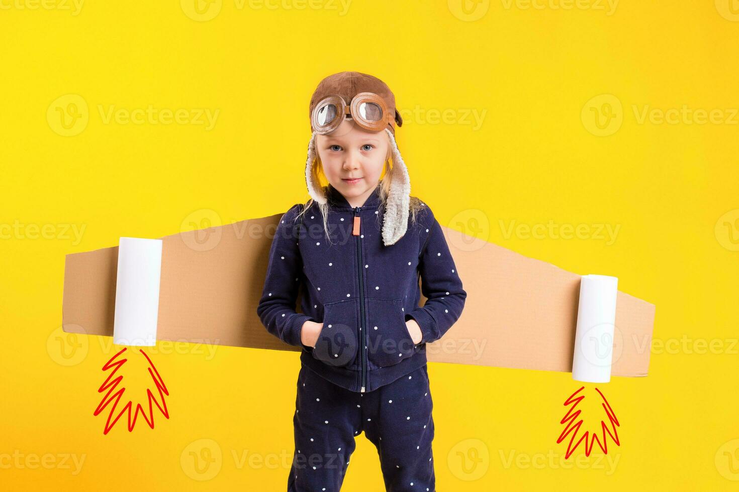frihet, flicka spelar till vara flygplan pilot, rolig liten flicka med flygare keps och glasögon, bär vingar tillverkad av brun kartong som ett flygplan foto
