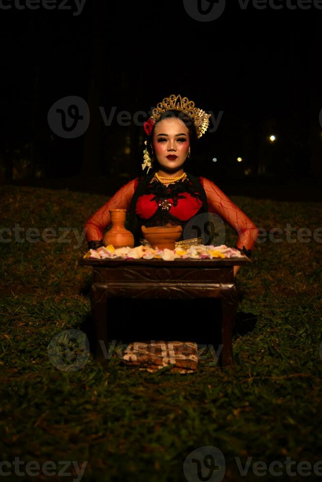 bred skott av ett asiatisk flicka i traditionell kläder Sammanträde i en skog med en tabell full av blommor foto