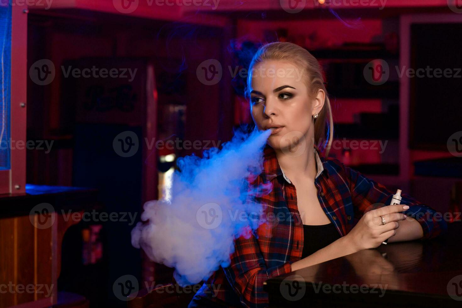 ung Söt kvinna i en skjorta i en bur rök ett elektronisk cigarett på de vape bar foto