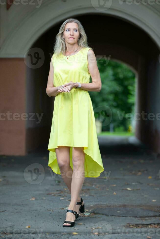 äldre smal kvinna blond i full tillväxt i en sommar gul klänning. foto