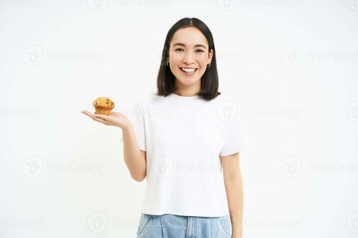 porträtt av leende koreanska kvinna, visar muffin i henne hand, isolerat på vit bakgrund foto