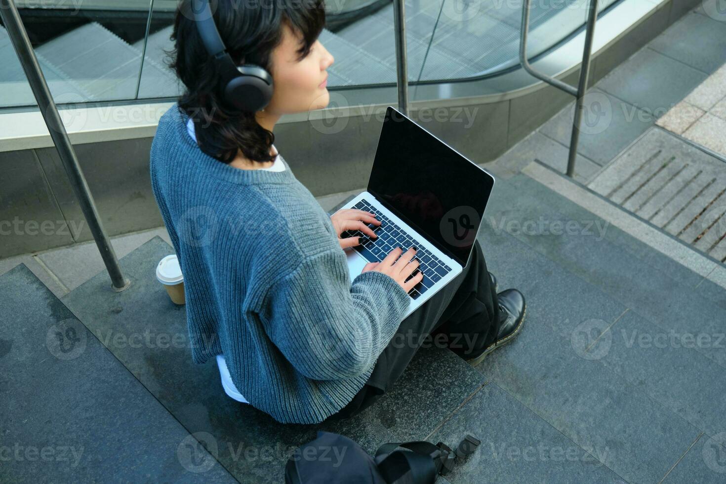 stänga upp porträtt av flicka, studerande Arbetar på bärbar dator och lyssnar musik i hörlurar. tom dator skärm och händer skriver på tangentbord foto