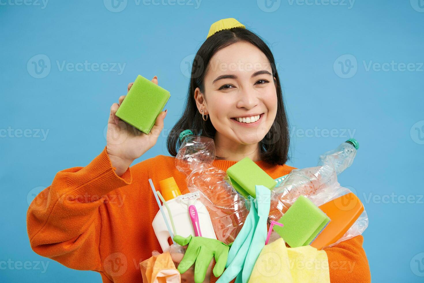 leende entusiastisk kvinna eco aktivist, innehav rengöring svamp, tömma plast flaskor och sopor, sortering avfall för återvinning, blå bakgrund foto