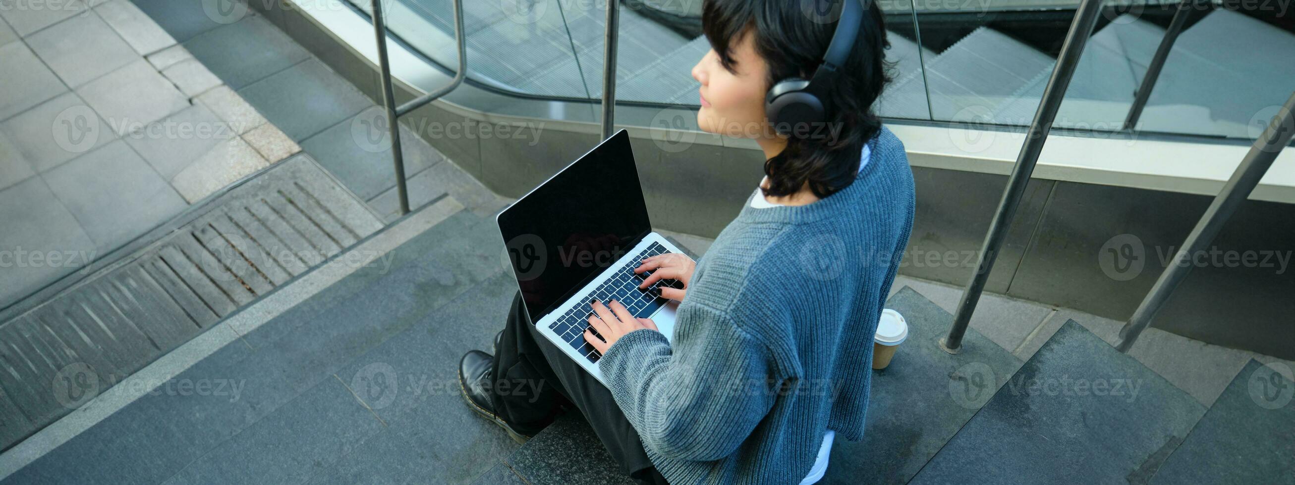 stänga upp porträtt av flicka, studerande Arbetar på bärbar dator och lyssnar musik i hörlurar. tom dator skärm och händer skriver på tangentbord foto