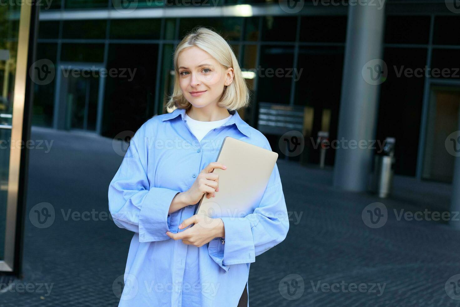 snygg, modern ung kvinna, studerande stående på gata i campus, rubrik till föreläsning med anteckningsbok och studie material, leende på kamera foto