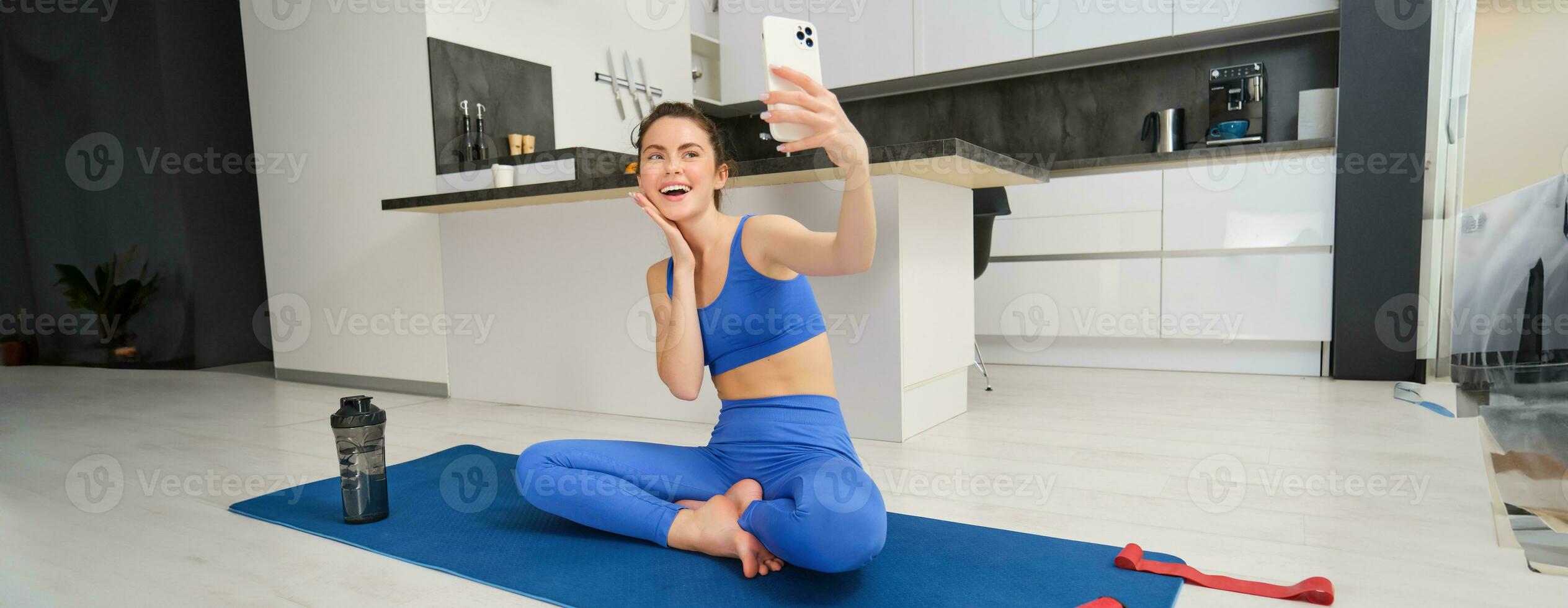 sport och livsstil begrepp. ung kvinna håller på med träna på Hem på yoga matta, gör kondition vlog med smartphone, tar selfie på mobil telefon foto