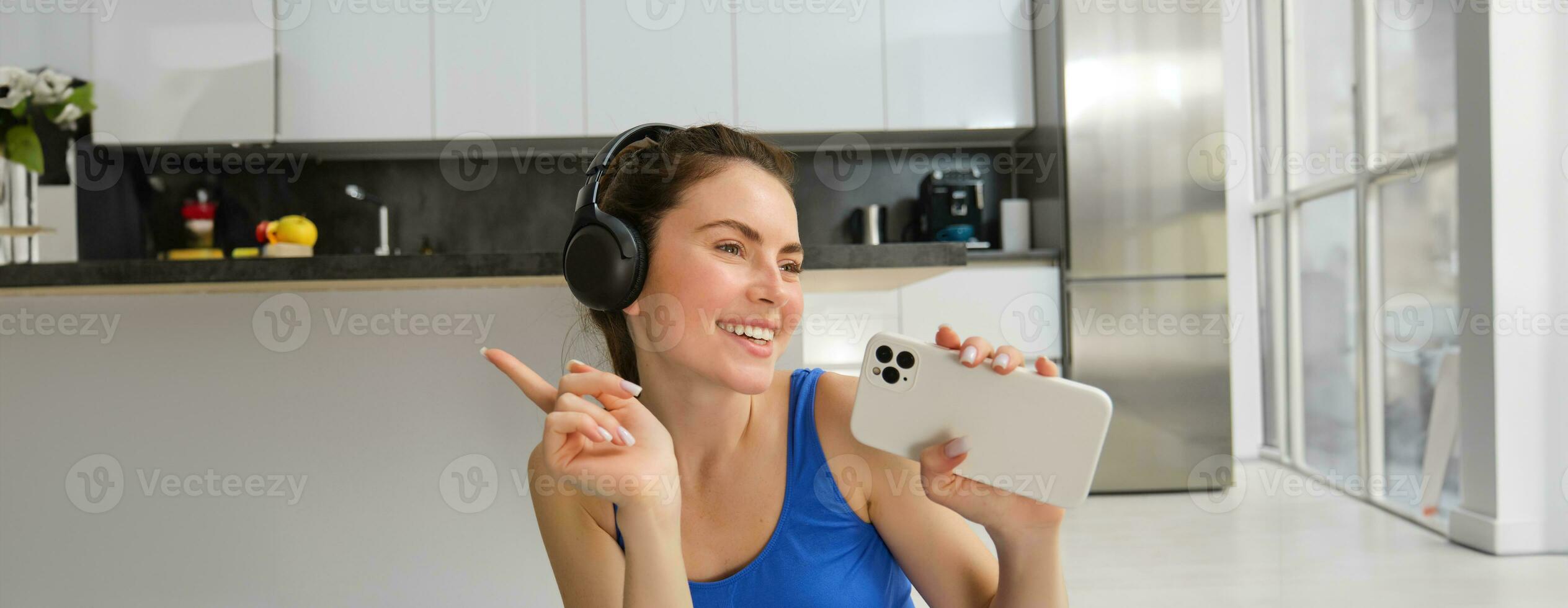 stänga upp porträtt av ung Lycklig kvinna, träna på Hem, lyssnar musik i trådlös hörlurar, sång på smartphone, håller på med Träning övningar foto