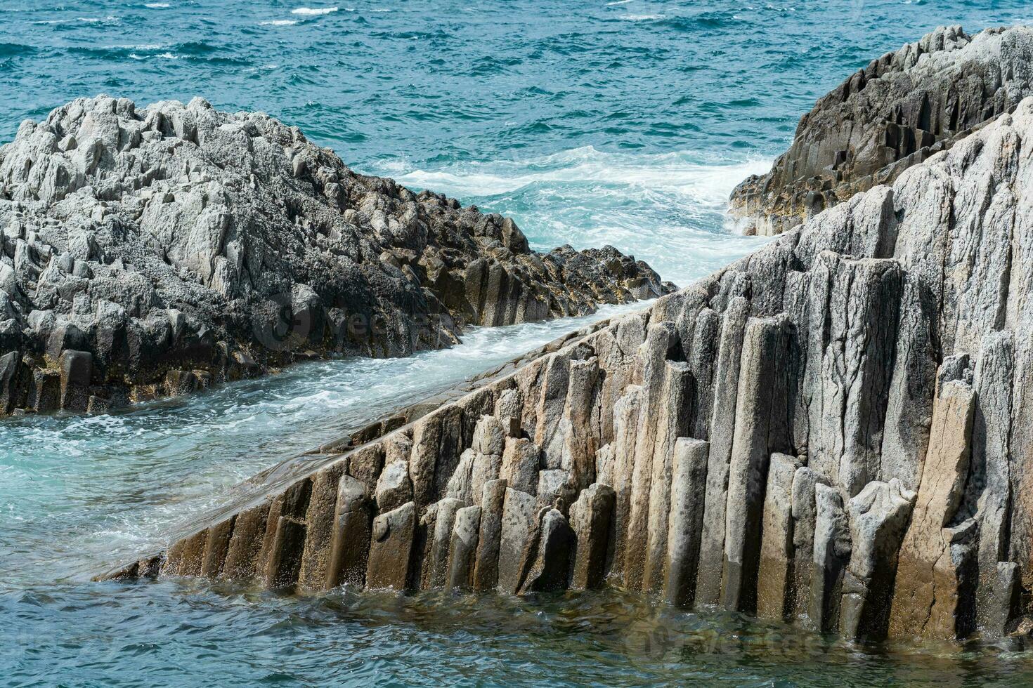 klippig havsstrand bildas förbi pelar- basalt mot de surfa, kust landskap av de kuril öar foto