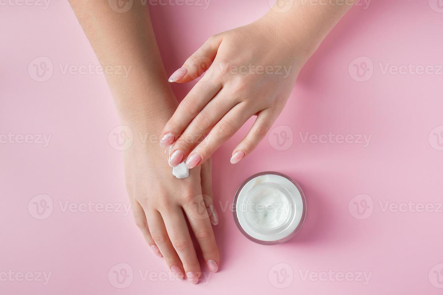 kvinnliga händer med en flaska grädde på rosa bakgrund. spa- och kroppsvårdskoncept. bild för reklam. foto