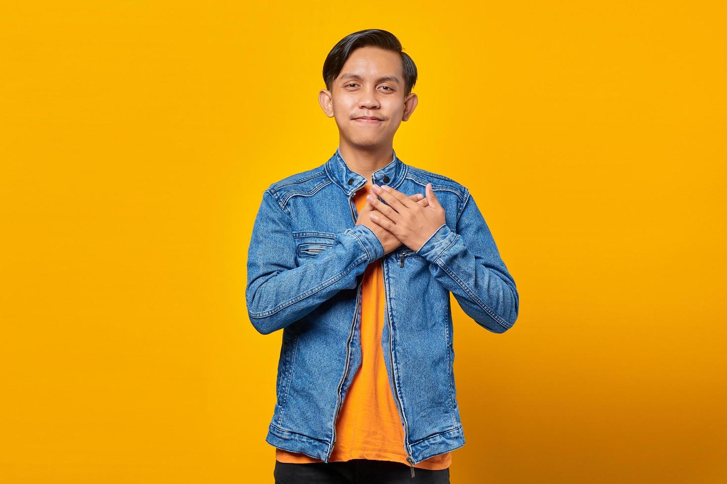 porträtt av leende asiatisk man med händerna på bröstet isolerad på gul bakgrund foto