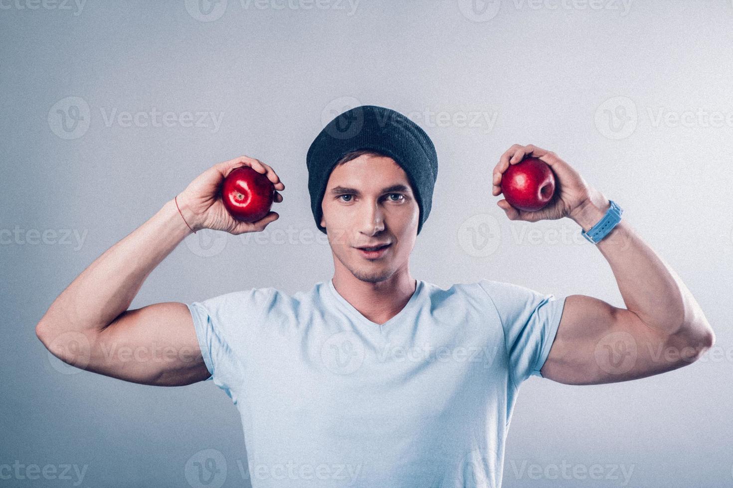ung man sport utseende visar muskler och håller äpplen i händerna foto