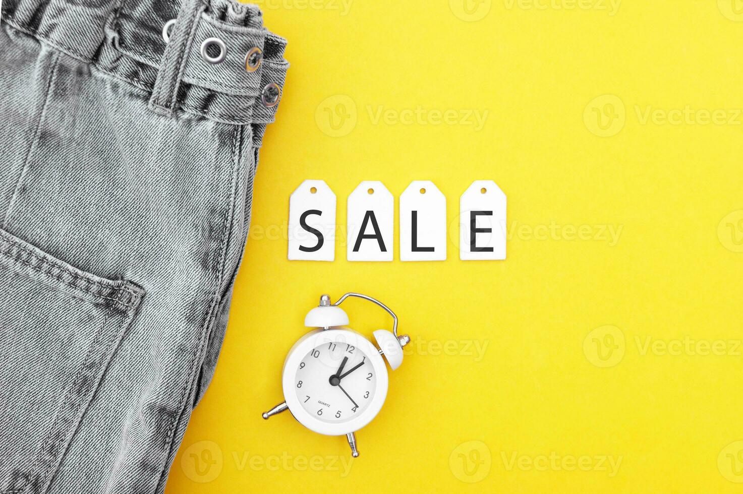 platt lägga, detalj av svart jeans, vit etiketter och inskrift försäljning på gul bakgrund. foto