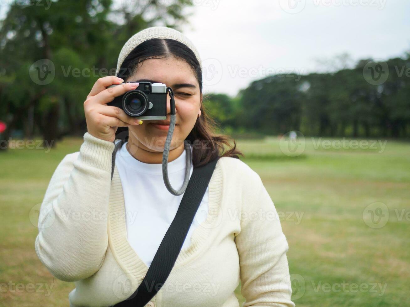 porträtt ung kvinna asiatisk knubbig söt skön ett person ha på sig svart skjorta se hand innehav använder sig av kamera i trädgård parkera utomhus- kväll solnedgång tid leende glad Lycklig koppla av sommar dag foto