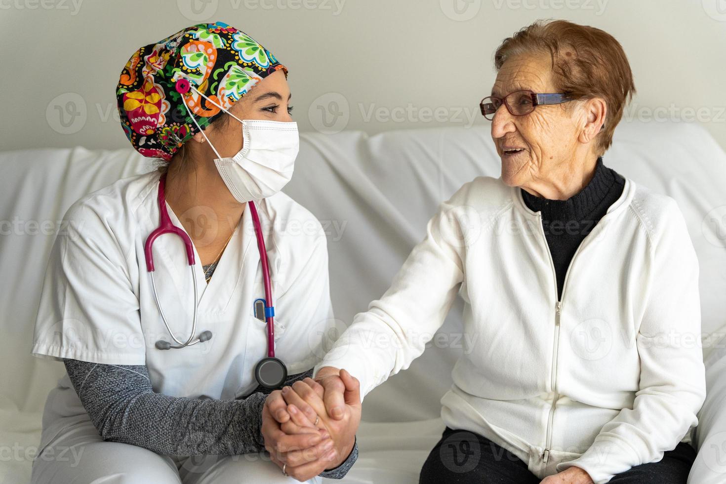 glad läkare i mask håller handen på äldre kvinna foto