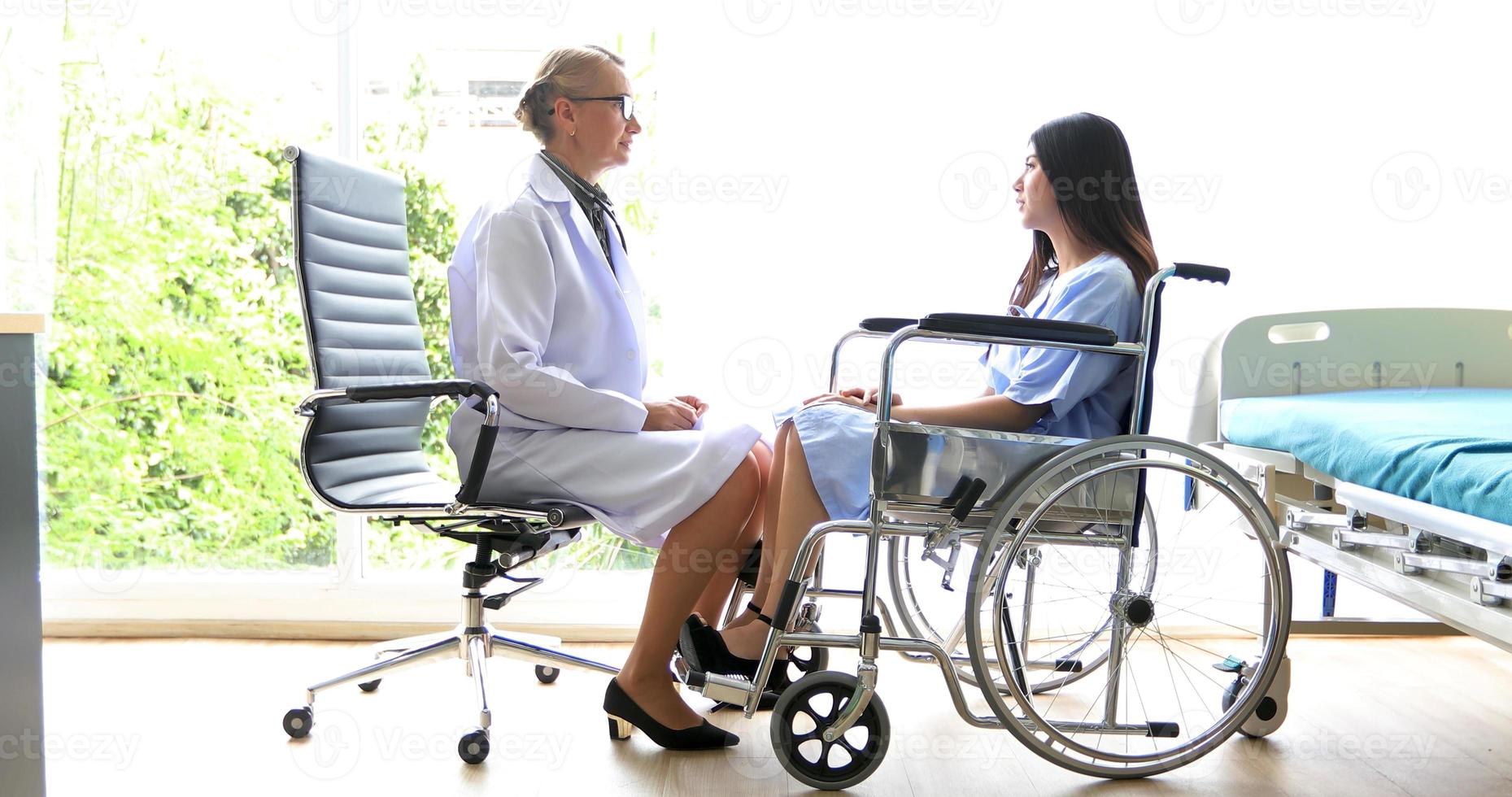 läkarna frågar och förklarar sjukdomen för en kvinnlig patient på rullstol på ett sjukhus foto