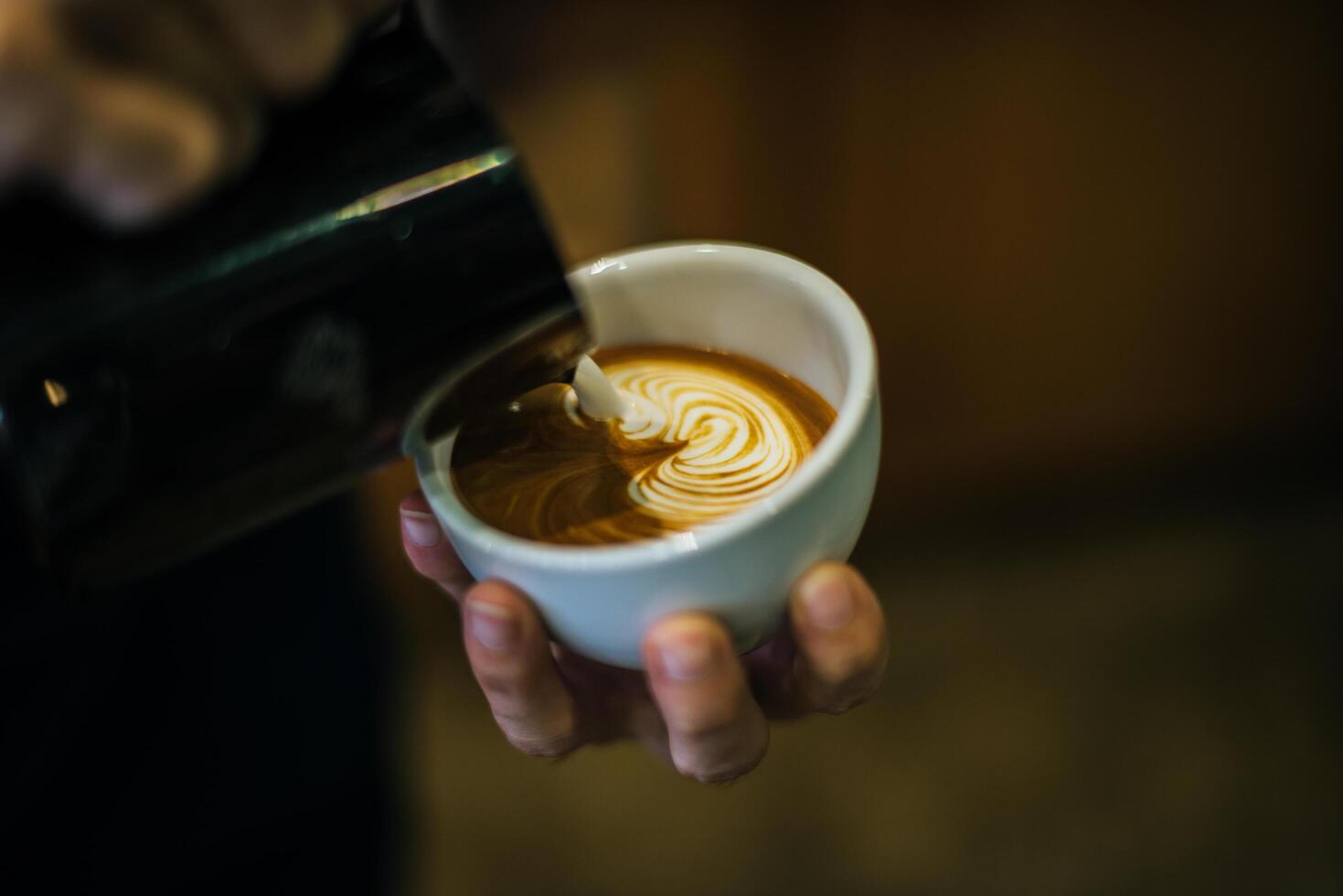 närbild av händer barista göra latte kaffe konst färg foto