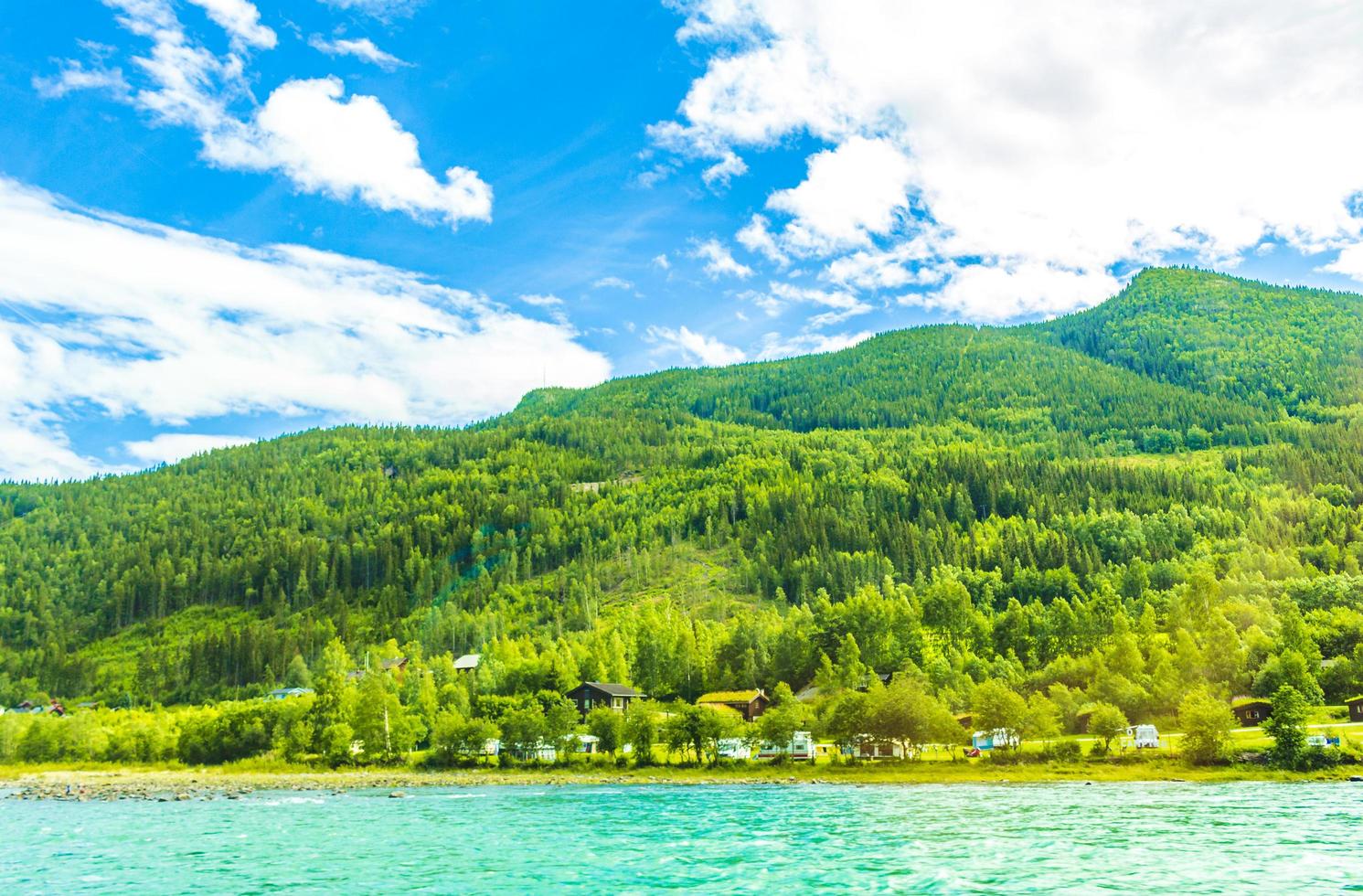 turkos smältvatten rinner i en flod genom byn i norge foto