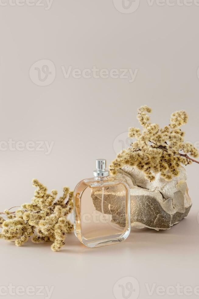 en chic flaska av kvinnors eller herr- parfym, en kosmetisk spray med en torr växt blomma på en pastell bakgrund med sten. vertikal se. foto