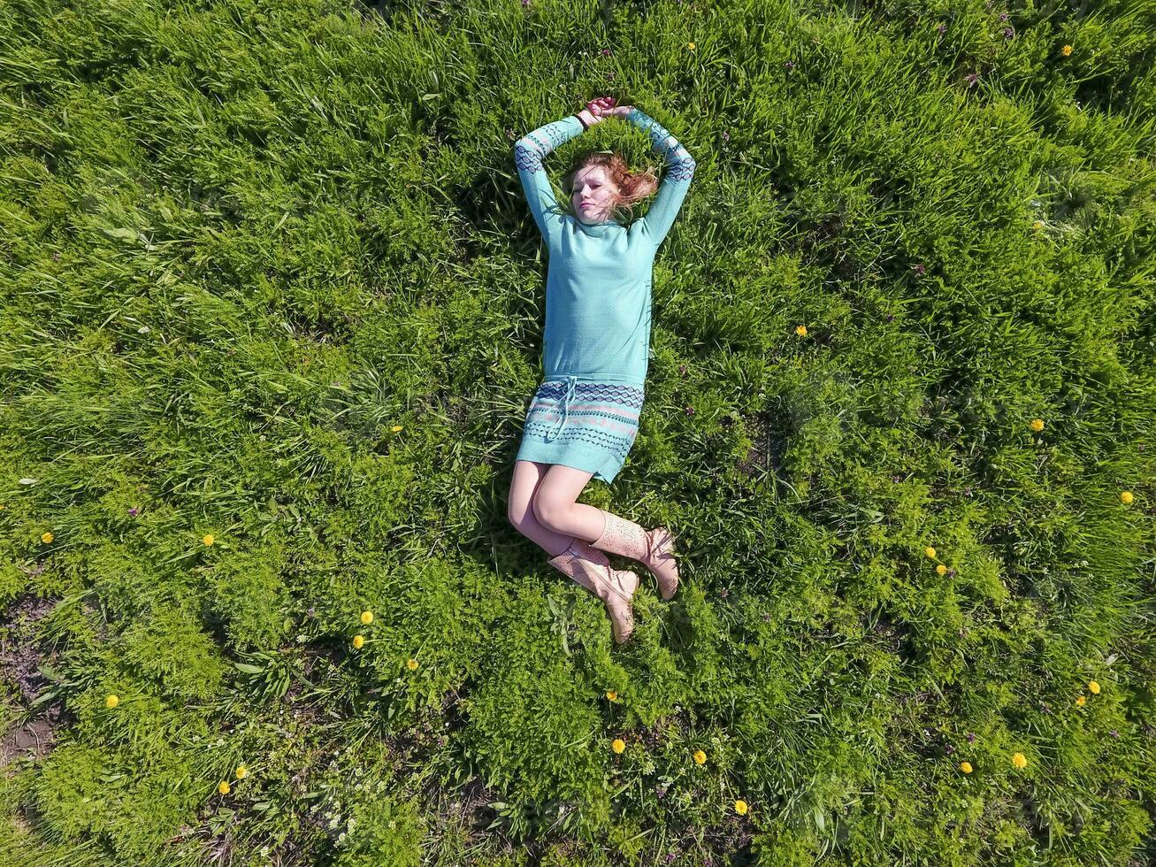 de flicka lögner i en turkos klänning på de gräsmatta. skön flicka liggande ner av gräs foto