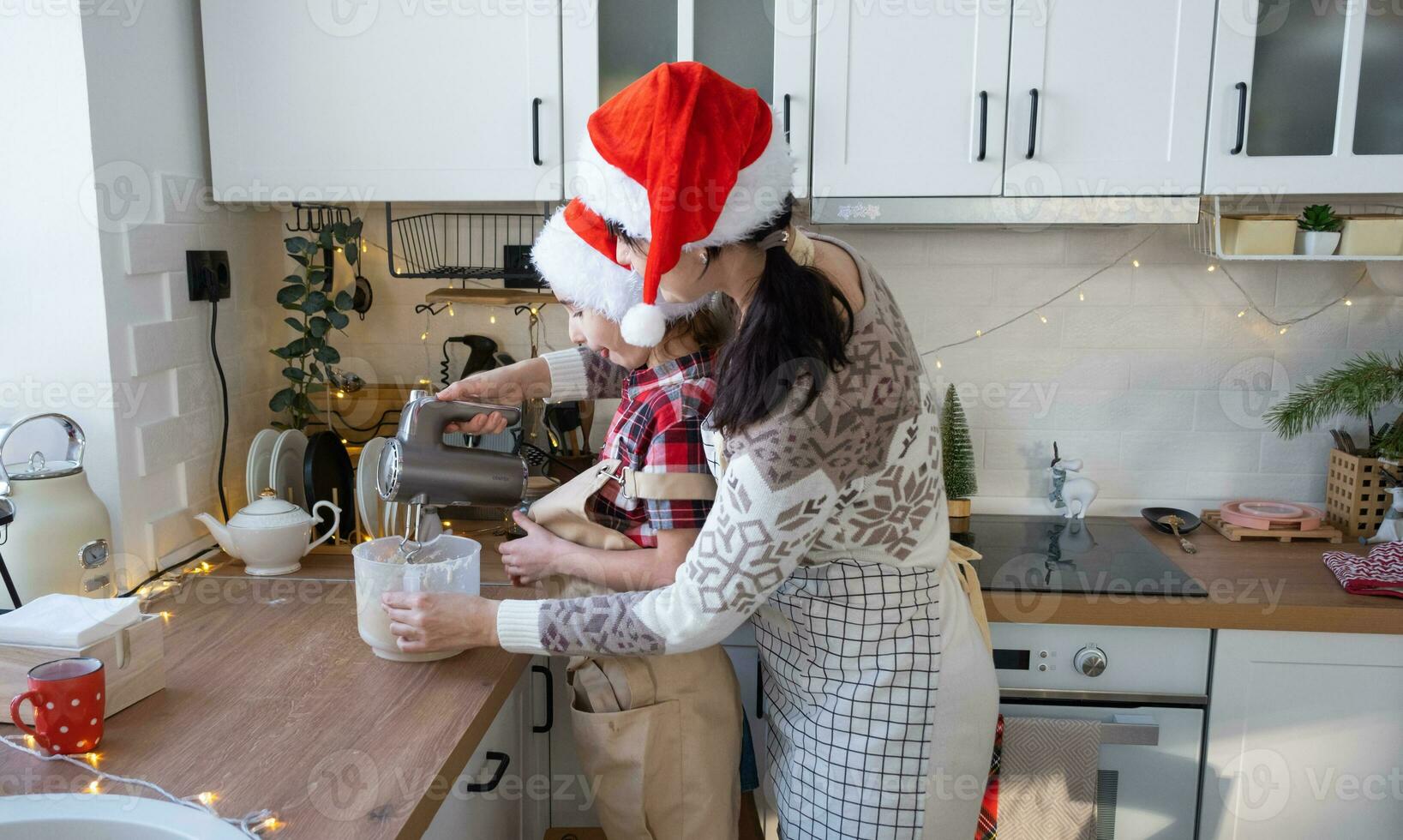 mamma och dotter i de vit kök knåda de deg i de skål för pepparkaka och småkakor med en blandare för jul och ny år. foto