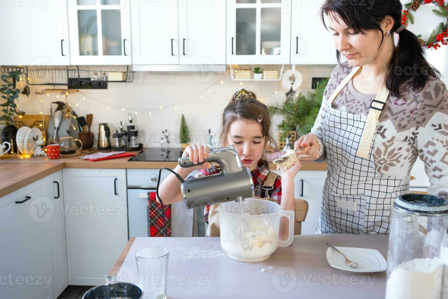 mamma och dotter i de vit kök knåda de deg i de skål för pepparkaka och småkakor med en blandare för jul och ny år. foto