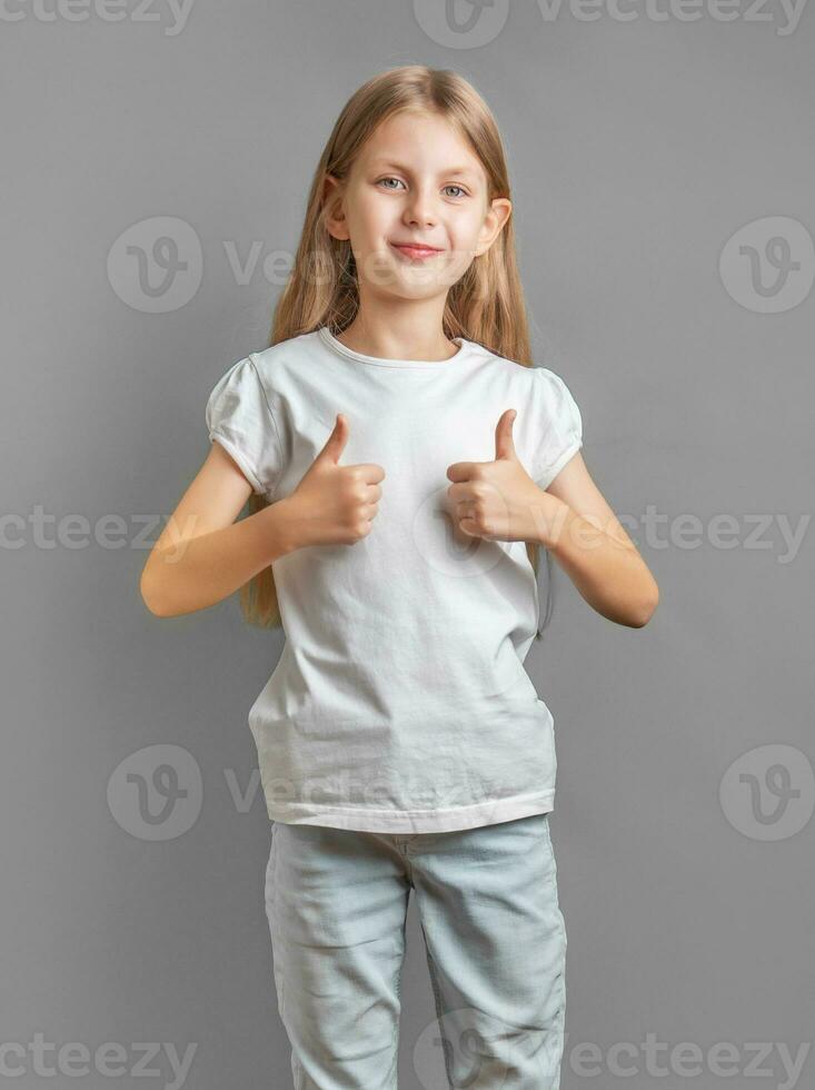 Lycklig barn, liten flicka som visar tummen upp gest i en vit t-shirt foto