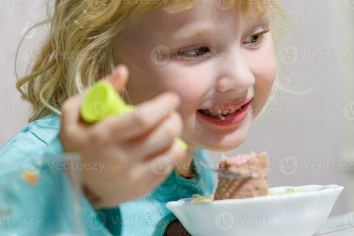 en liten flicka har frukost på Hem spaghetti med korvar. liten blond flicka äter middag med gaffel på tabell foto